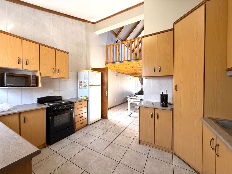 A functional kitchen featuring laminate cabinetry, tiled splashbacks, and a freestanding oven, with an open-plan layout leading to a mezzanine level.