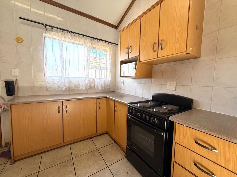 A functional kitchen featuring light wood-look cabinetry, tiled splashbacks, tiled flooring, and a freestanding electric stove with oven.