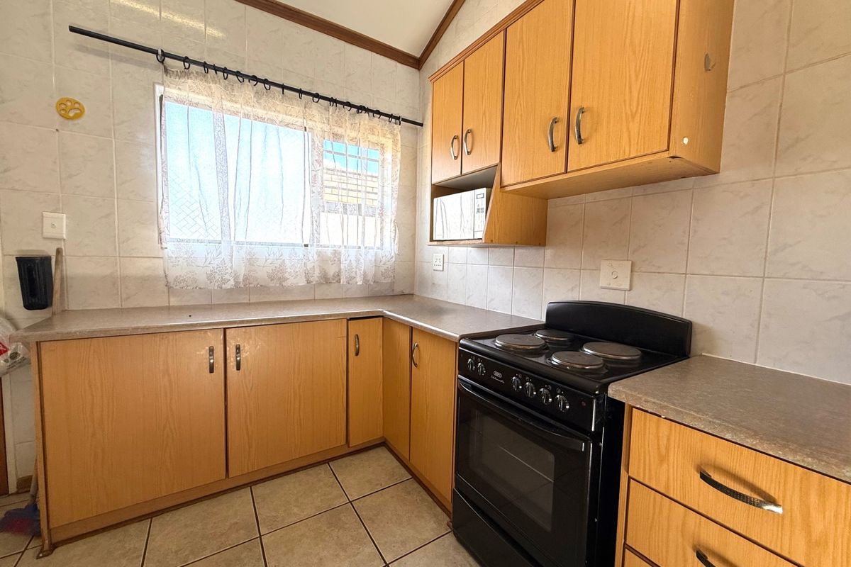 A functional kitchen featuring light wood-look cabinetry, tiled splashbacks, tiled flooring, and a freestanding electric stove with oven.