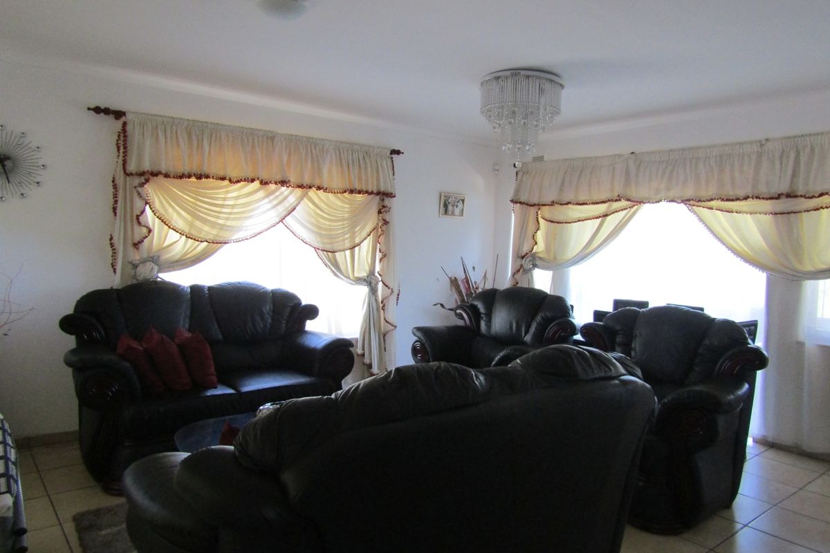A spacious living room featuring tiled flooring and a decorative crystal chandelier, offering a bright and comfortable area for relaxation.