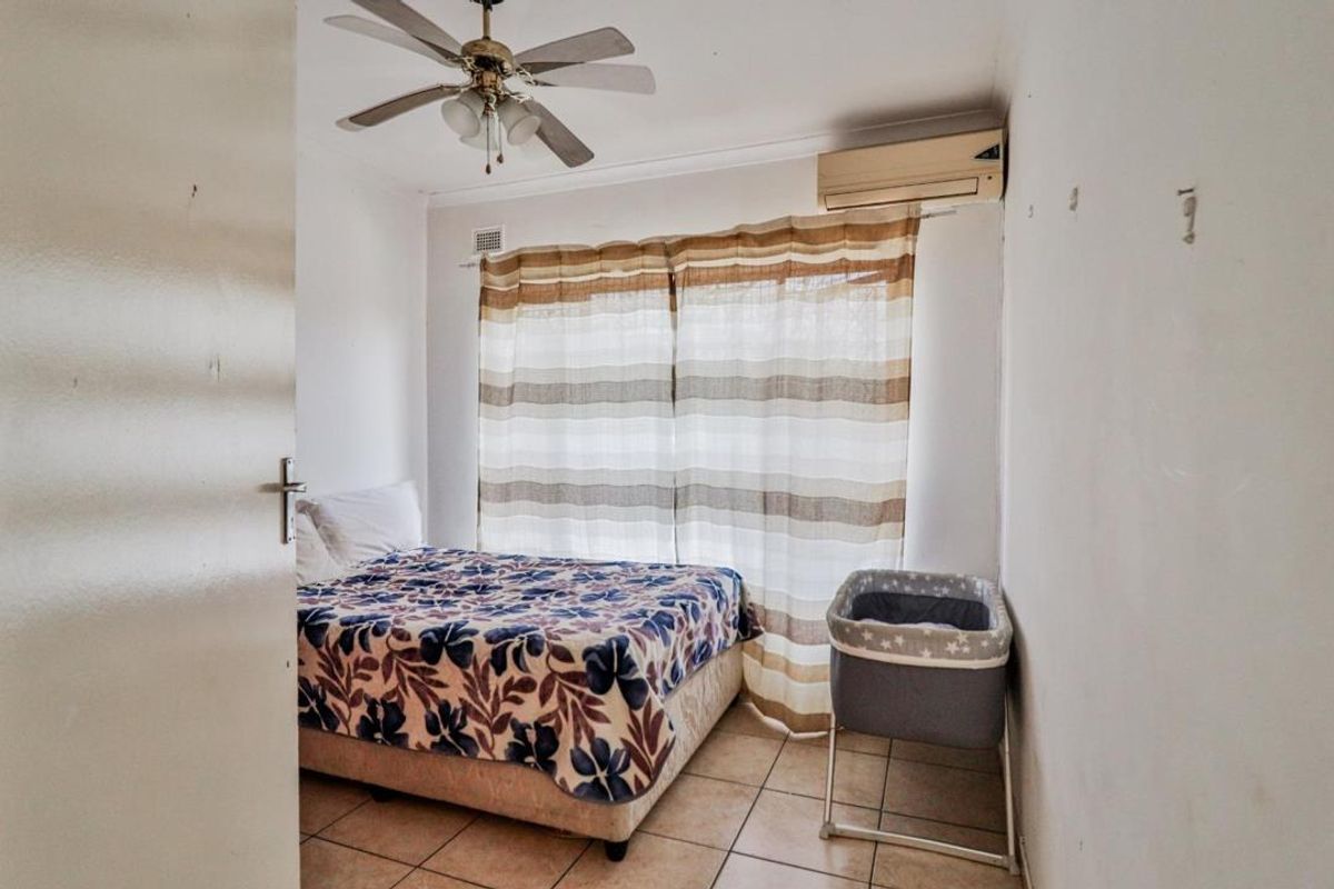 A functional bedroom featuring tiled flooring, a ceiling fan, and a wall-mounted split-system air conditioner.