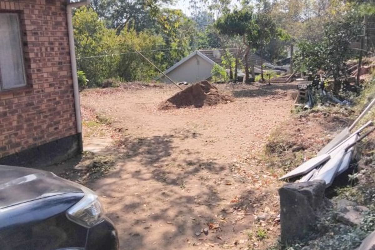 A view of the rear exterior area showing a face brick wall and an unlandscaped yard with loose soil and debris.