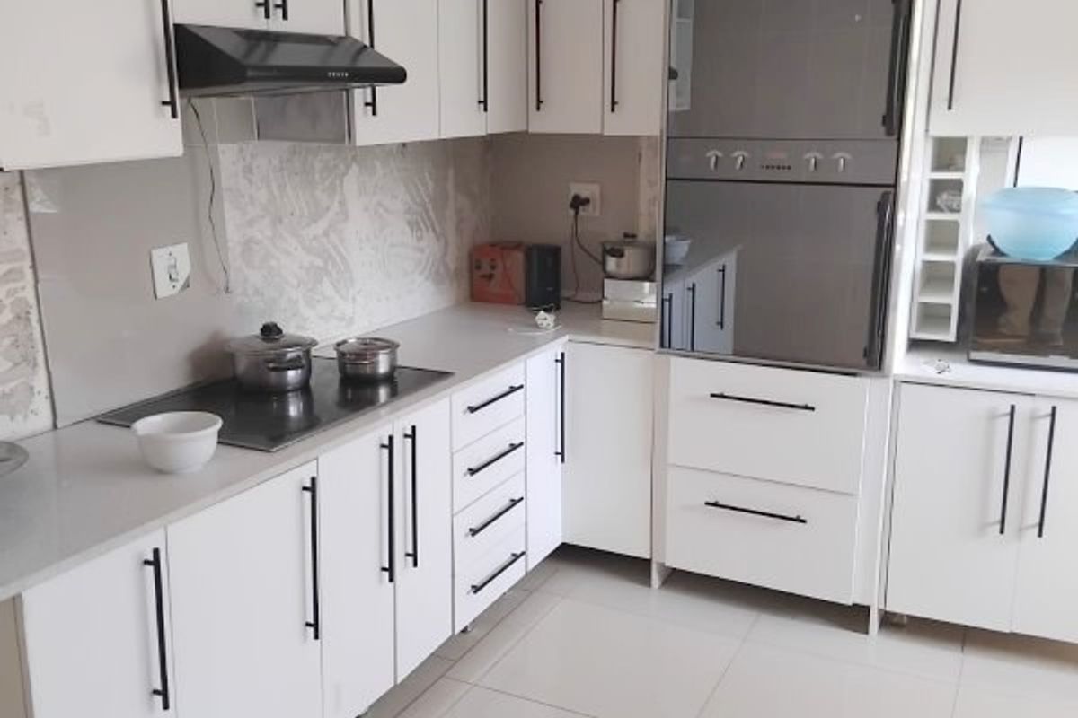 Modern kitchen featuring white cabinetry, stone countertops, integrated oven, and electric hob with a tiled backsplash and floor.