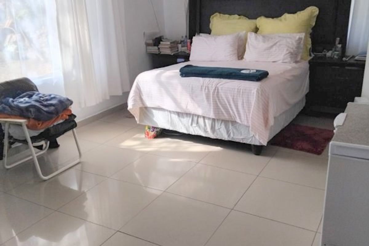 A spacious bedroom featuring neutral tiled flooring and large windows with curtain tracks, offering a clean and functional living space.