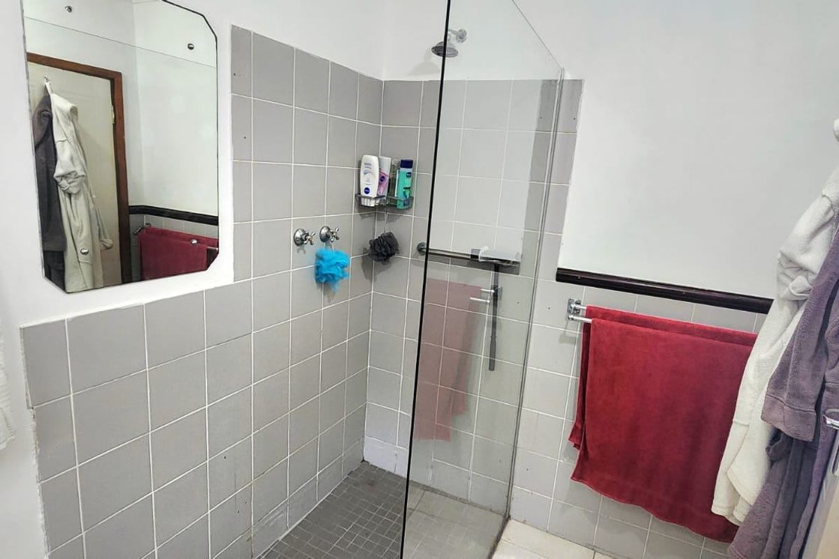 A functional bathroom featuring a walk-in shower with a glass screen, wall-mounted mirror, and tiled finishes.
