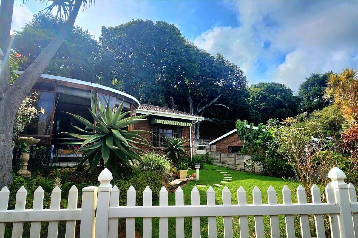 A view of the rear garden featuring a brick townhouse facade, a curved patio enclosure, and a well-maintained lawn with a paved pathway.