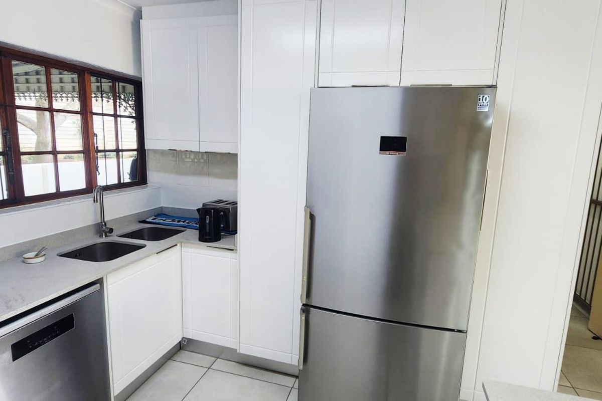 Modern kitchen featuring white cabinetry, stone countertops, double basin sink, and integrated dishwasher, complemented by tiled flooring and natural light.