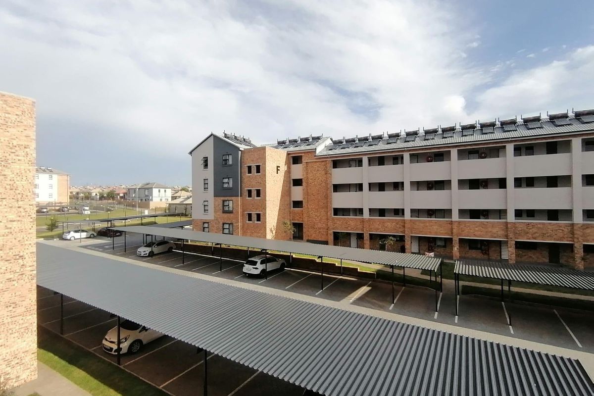 Elevated view of an apartment complex featuring facebrick architecture, covered parking bays, and roof-mounted solar water heating panels.