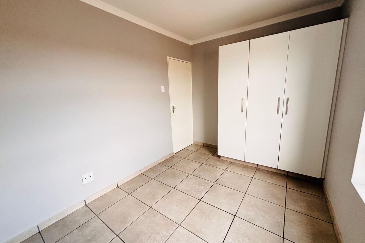 A clean, empty bedroom featuring neutral wall paint, tiled flooring, and a white built-in wardrobe with modern handles.