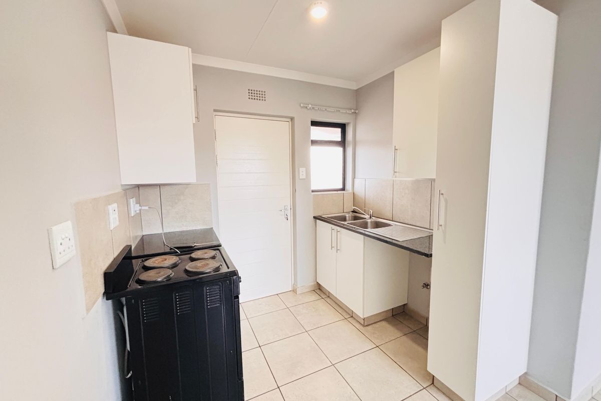 A functional kitchen featuring white cabinetry, tiled splashbacks, a double sink, and a freestanding electric stove, offering a clean and practical workspace.