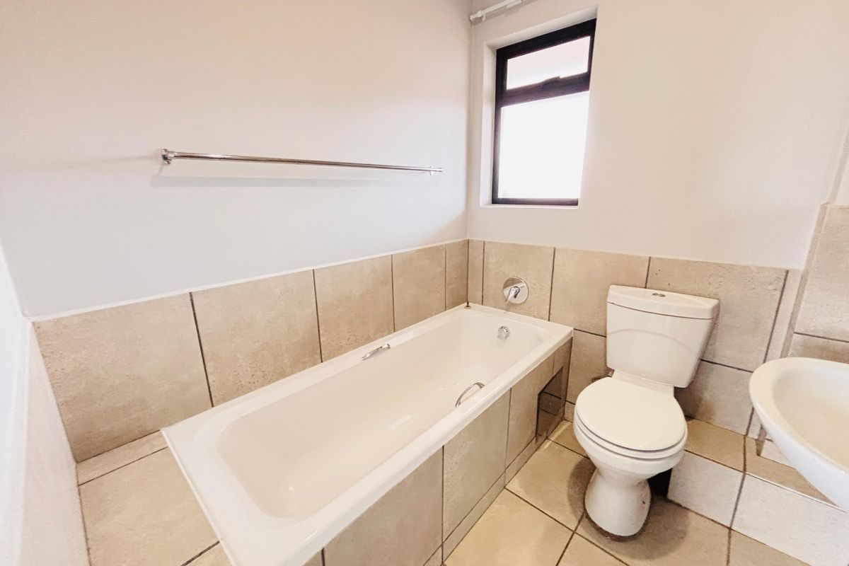 A clean, functional bathroom featuring a built-in bathtub, standard toilet, and wall-mounted washbasin with neutral floor and wall tiling.
