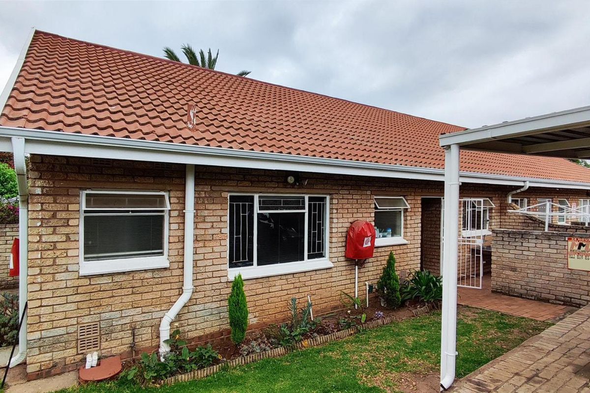 Rear exterior view of the townhouse featuring face brick construction, a tiled roof, security bars on windows, and a paved patio area.