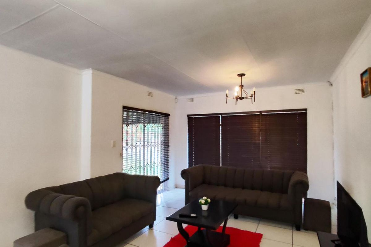 A living room featuring tiled flooring, dark venetian blinds, and a security gate leading to the exterior.