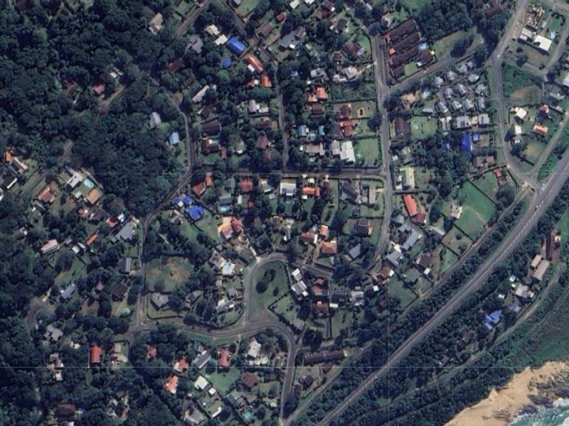 Aerial view of a residential vacant land plot highlighted in red, situated within a established coastal neighborhood.