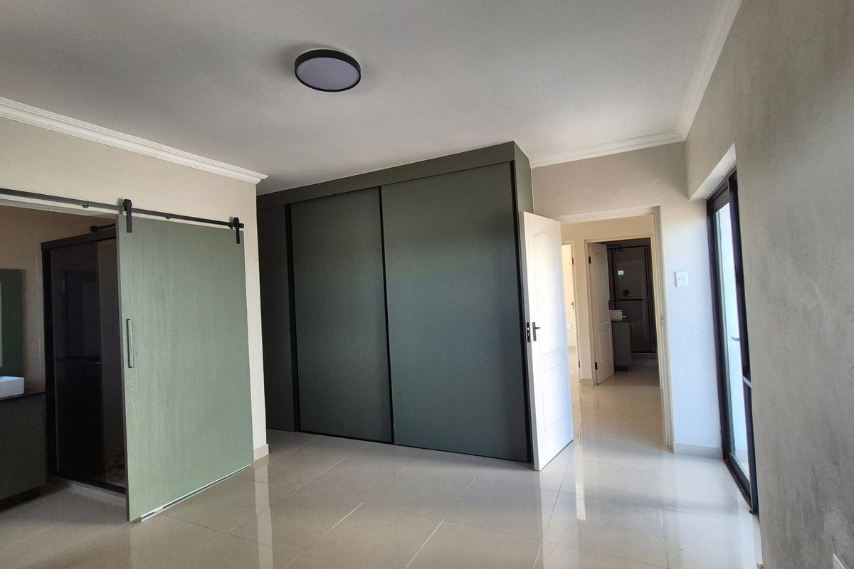 Spacious bedroom featuring modern tiled flooring, a large built-in sliding wardrobe, and a sliding barn door leading to an en-suite bathroom.