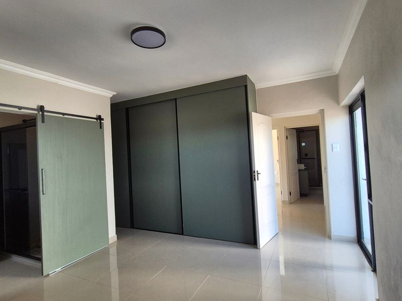 Spacious bedroom featuring modern tiled flooring, a large built-in sliding wardrobe, and a sliding barn door leading to an en-suite bathroom.