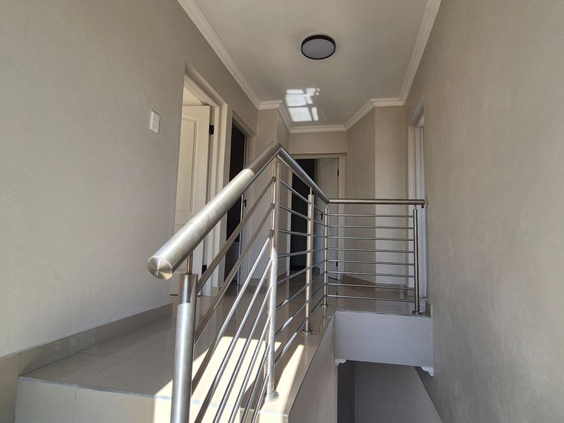 A bright, modern hallway featuring tiled flooring and a sleek stainless steel balustrade leading to the upper level.