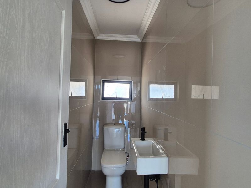 A modern, compact guest bathroom featuring neutral ceramic wall tiles, a wall-mounted basin with a black mixer tap, and a clean, minimalist design.