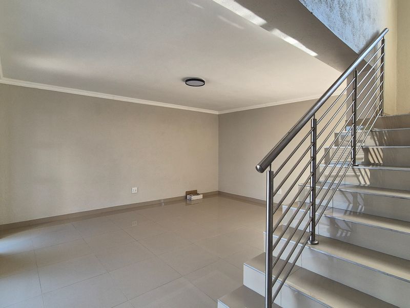Spacious open-plan living area featuring neutral tiled flooring, a modern staircase with stainless steel balustrades, and large sliding glass doors for natural light.