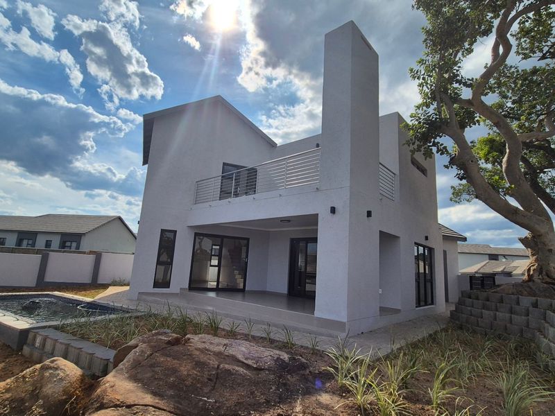 Rear view of a modern two-story house featuring a covered patio, upper balcony with stainless steel balustrade, and a private swimming pool.