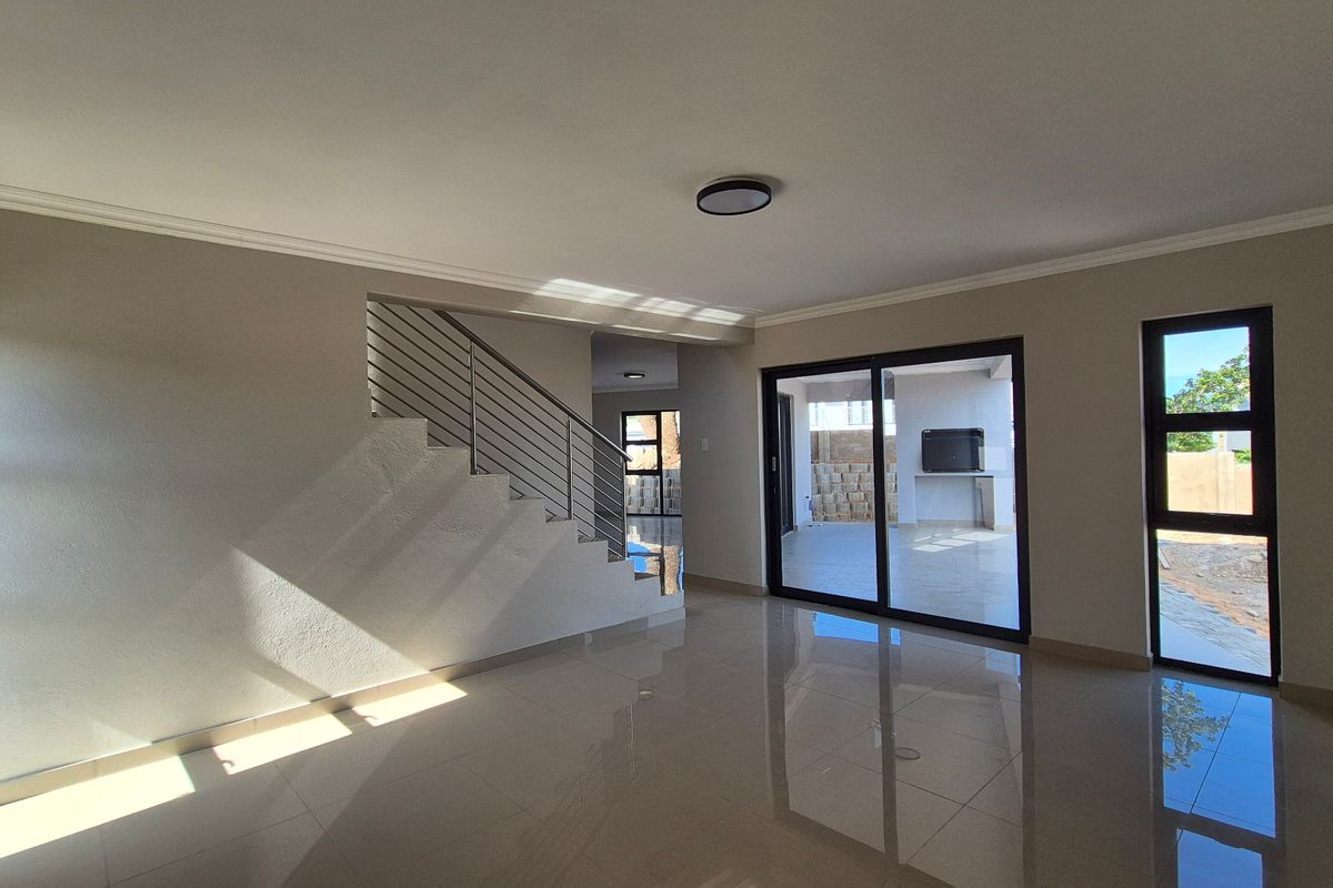 Spacious open-plan living area featuring polished tile flooring, a modern staircase with stainless steel balustrade, and large sliding doors leading to an outdoor patio.