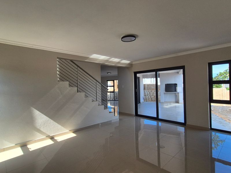 Spacious open-plan living area featuring polished tile flooring, a modern staircase with stainless steel balustrade, and large sliding doors leading to an outdoor patio.
