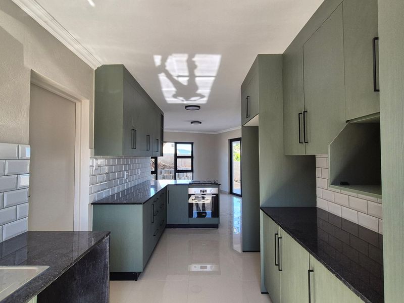 Modern kitchen featuring sage green cabinetry, dark stone countertops, white subway tile backsplash, and integrated appliances with polished floor tiles.