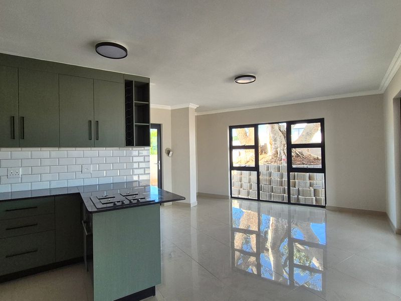 Modern open-plan kitchen and living area featuring olive green cabinetry, subway tile backsplash, stone countertops, and large sliding doors leading to the exterior.