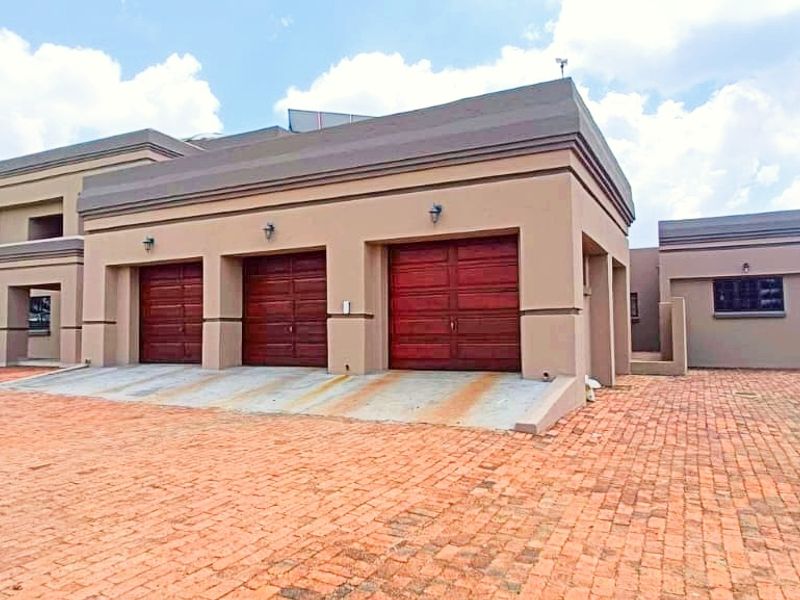 A modern farm-style property featuring a triple garage with wooden doors, a spacious brick-paved driveway, and well-maintained exterior finishes.