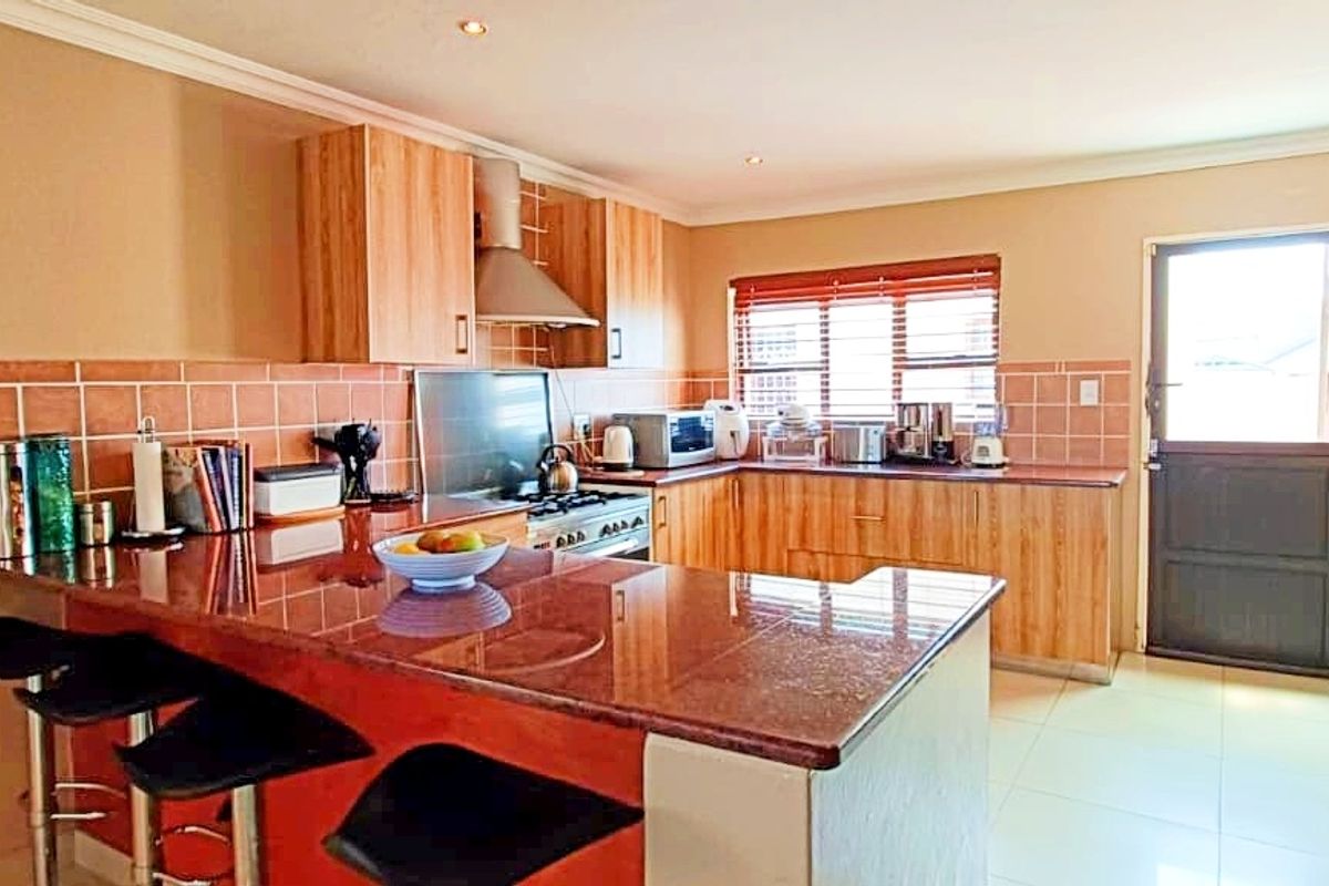 A functional kitchen featuring granite countertops, wooden cabinetry, a tiled backsplash, and a breakfast bar area with direct access to the exterior.