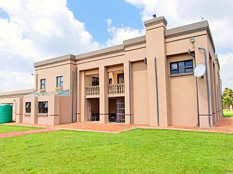 Rear view of a multi-story farm residence featuring a brick paved patio, upper-level balcony, and expansive surrounding lawn area.