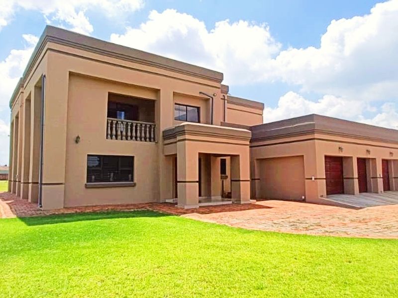 A modern double-story farm residence featuring a triple garage, paved driveway, and an upper-level balcony set within a spacious landscaped garden.