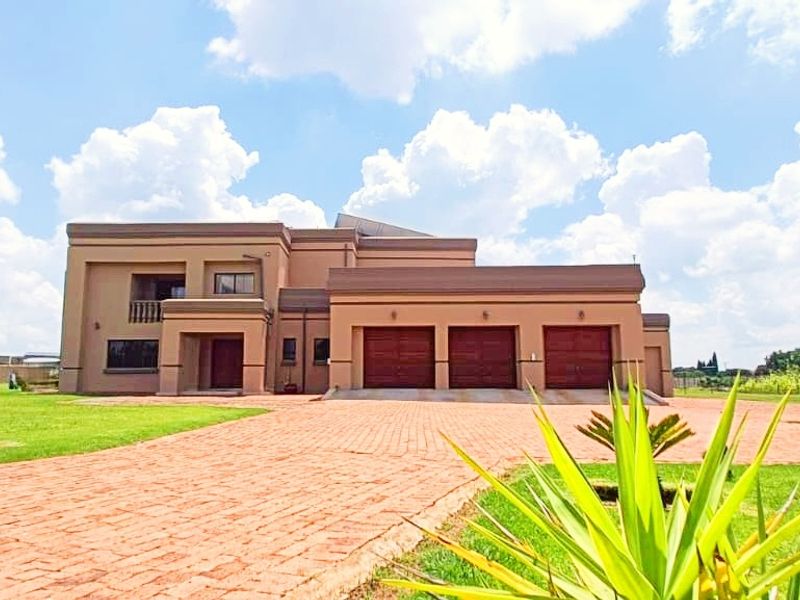 A spacious double-story farm residence featuring a triple garage, extensive paved driveway, and well-maintained surrounding lawns under a clear sky.