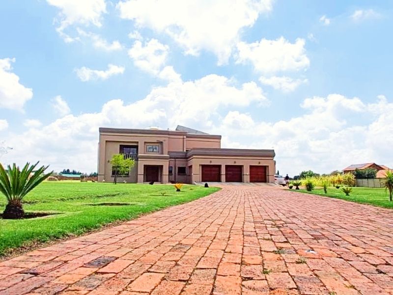 Front view of a modern farm property featuring a long brick-paved driveway, expansive lawn, and a triple garage.