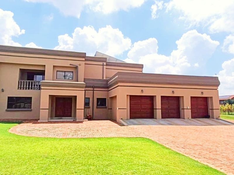 A spacious double-story farm residence featuring a triple garage, paved driveway, and a front balcony, set within a large, well-maintained lawn area.