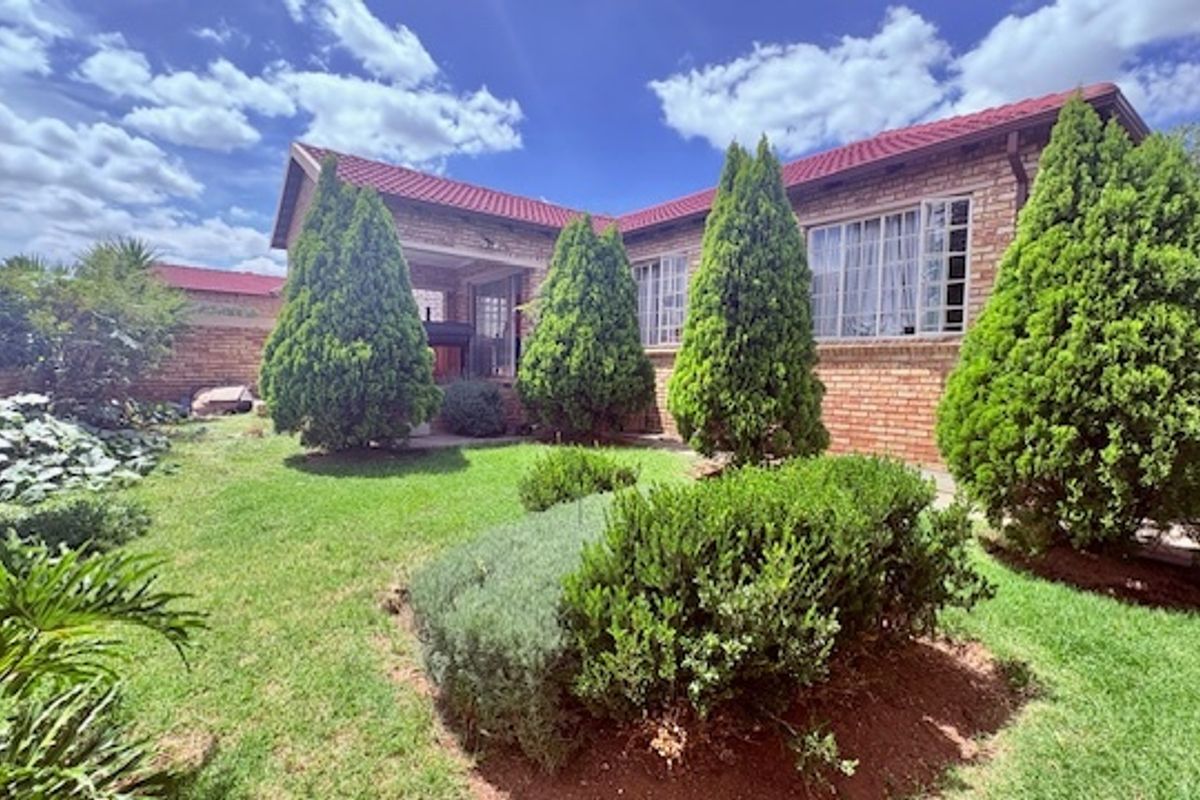 A view of the rear garden and exterior brick facade of the cluster home, featuring a lawn and established landscaping.