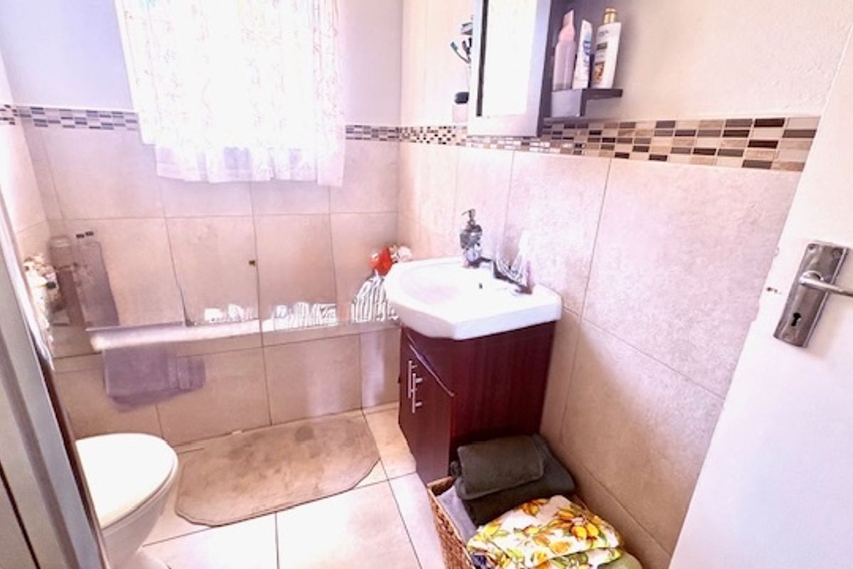 A compact bathroom featuring a vanity basin, tiled walls with decorative mosaic accents, and a shower area.