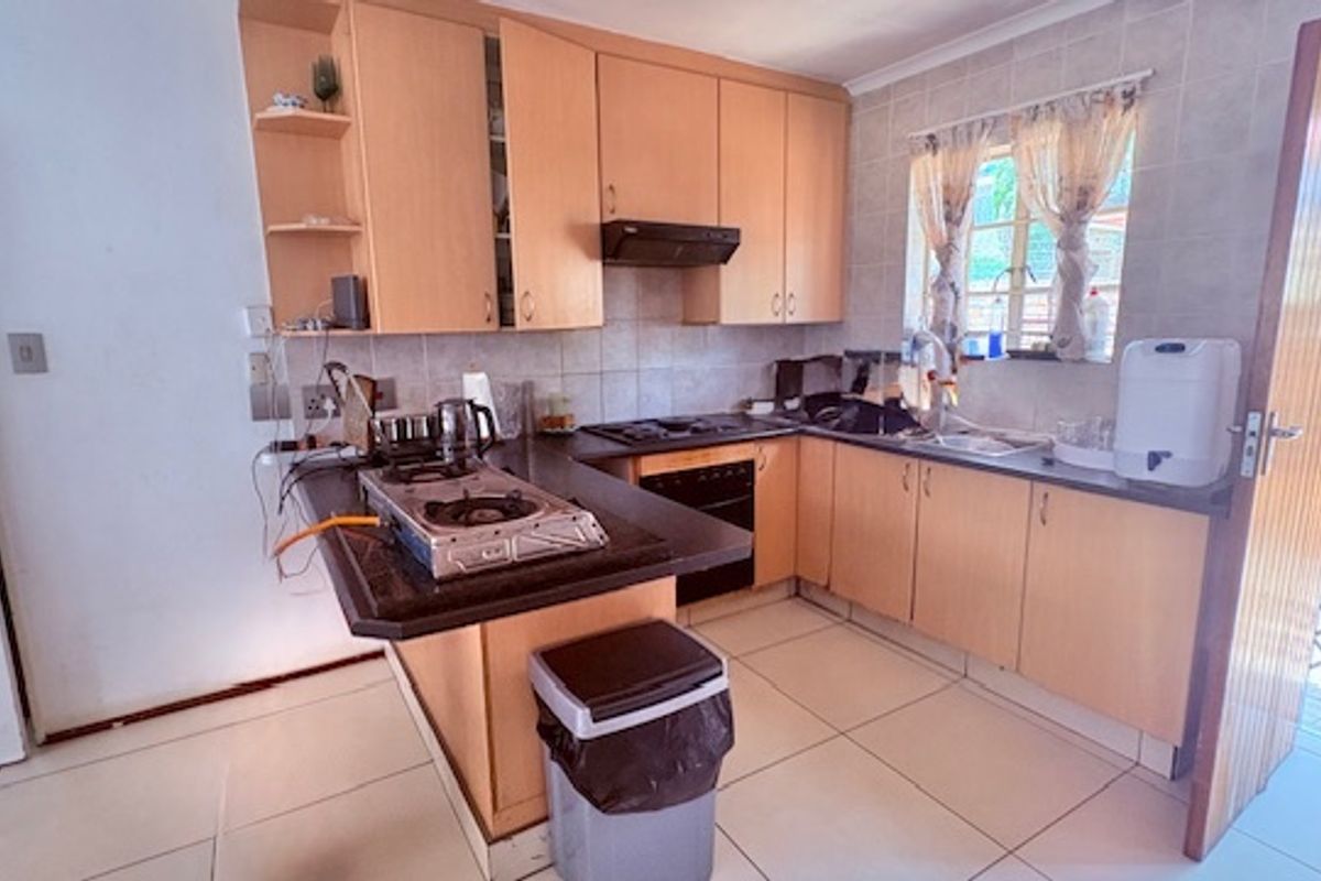 A functional kitchen featuring light wood cabinetry, dark countertops, a built-in oven, and a gas hob, with tiled flooring throughout.