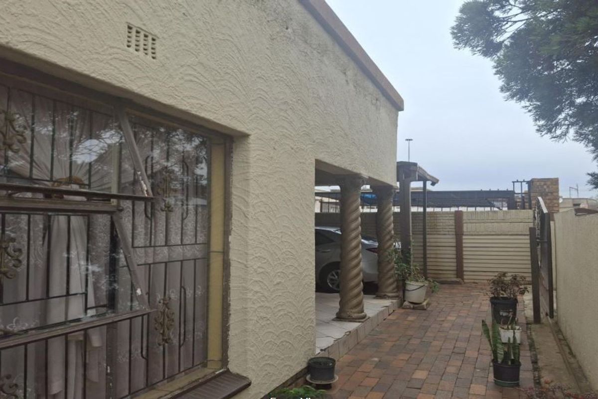 Side view of the property featuring a textured plaster facade, decorative spiral columns, and a paved driveway area with perimeter boundary walling.