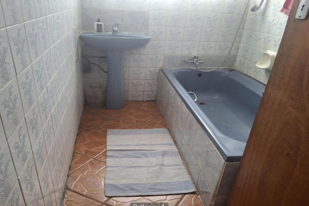 A dated bathroom featuring a blue pedestal basin and matching built-in bathtub with full-height wall tiling and tiled flooring.