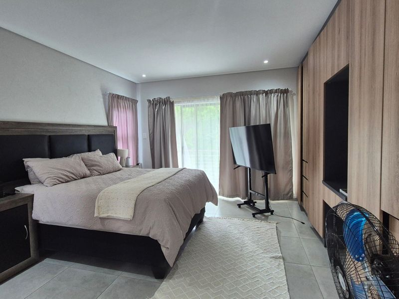 A well-maintained bedroom featuring modern built-in cupboards, neutral tiled flooring, and recessed lighting, offering a clean and functional living space.