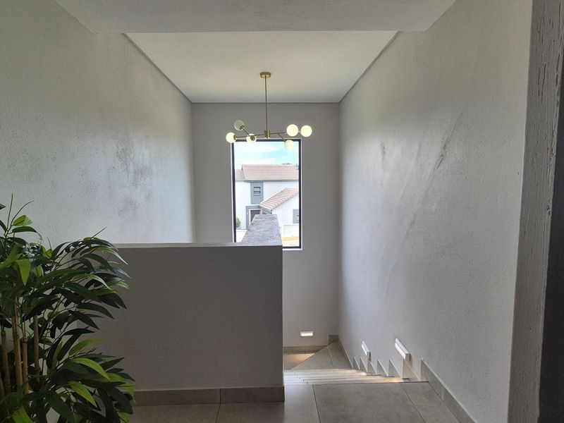 A bright and modern hallway featuring a staircase with recessed wall lighting, tiled floors, and a contemporary chandelier.