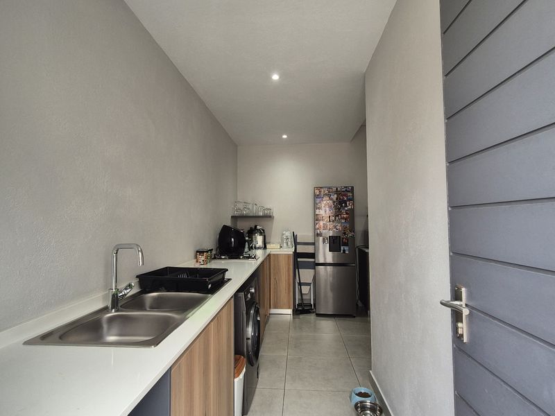 A functional scullery featuring a double stainless steel sink, stone countertops, and ample built-in cabinetry with modern tiled flooring.