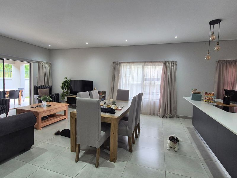 Spacious open-plan living and dining area featuring modern tiled flooring, recessed lighting, and a functional kitchen island with direct access to the patio.