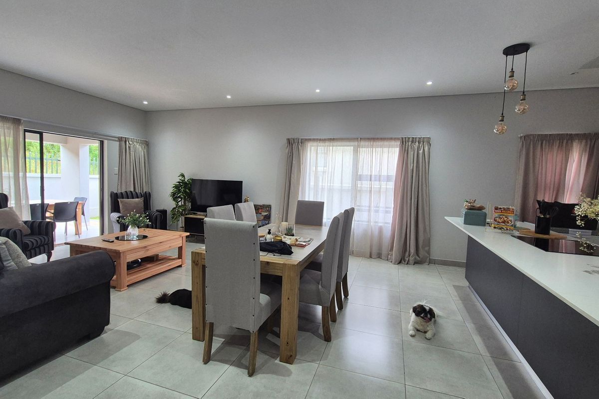 Spacious open-plan living and dining area featuring modern tiled flooring, recessed lighting, and a functional kitchen island with direct access to the patio.