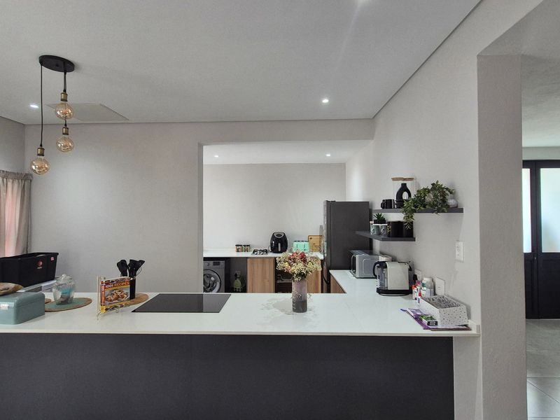 Modern open-plan kitchen featuring a central island with an induction cooktop, sleek cabinetry, and recessed lighting, seamlessly connecting to the adjacent living and utility areas.