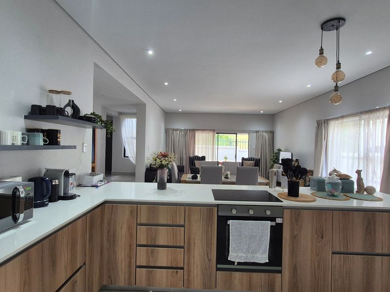 Modern open-plan kitchen featuring wood-grain cabinetry, stone countertops, and integrated appliances, flowing seamlessly into the dining and living areas.