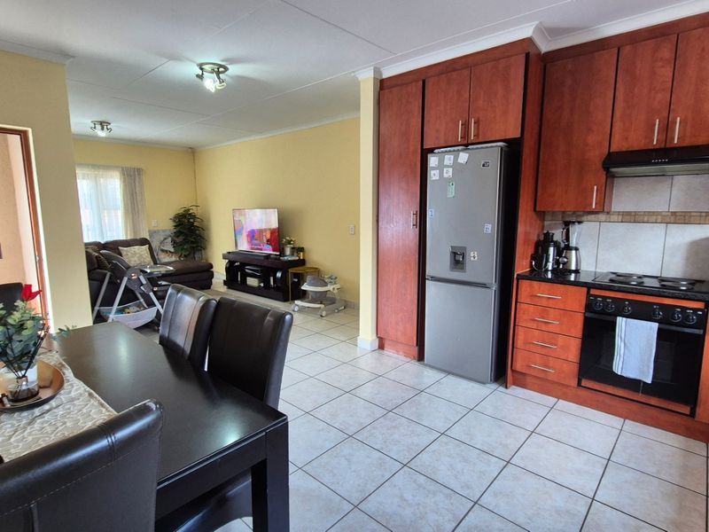 Open-plan living and kitchen area featuring tiled flooring, wooden cabinetry, and integrated cooking appliances, creating a functional and connected family space.