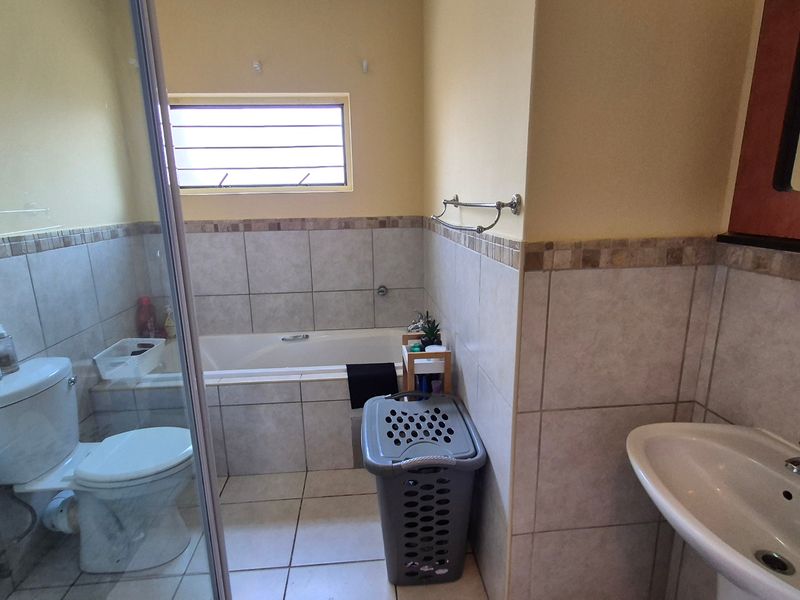 A functional bathroom featuring a shower enclosure, bathtub, pedestal basin, and tiled finishes throughout.
