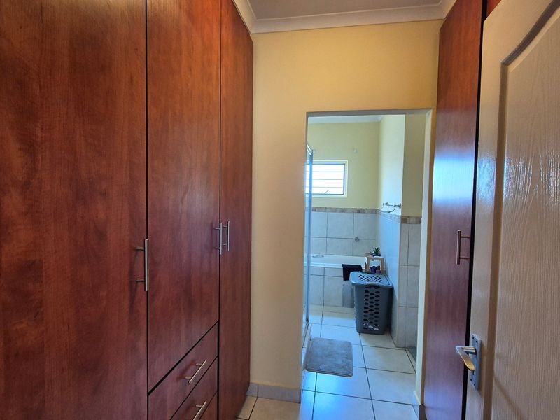 A hallway featuring extensive built-in wooden cabinetry and tiled flooring, providing a transition space leading into an adjacent bathroom.